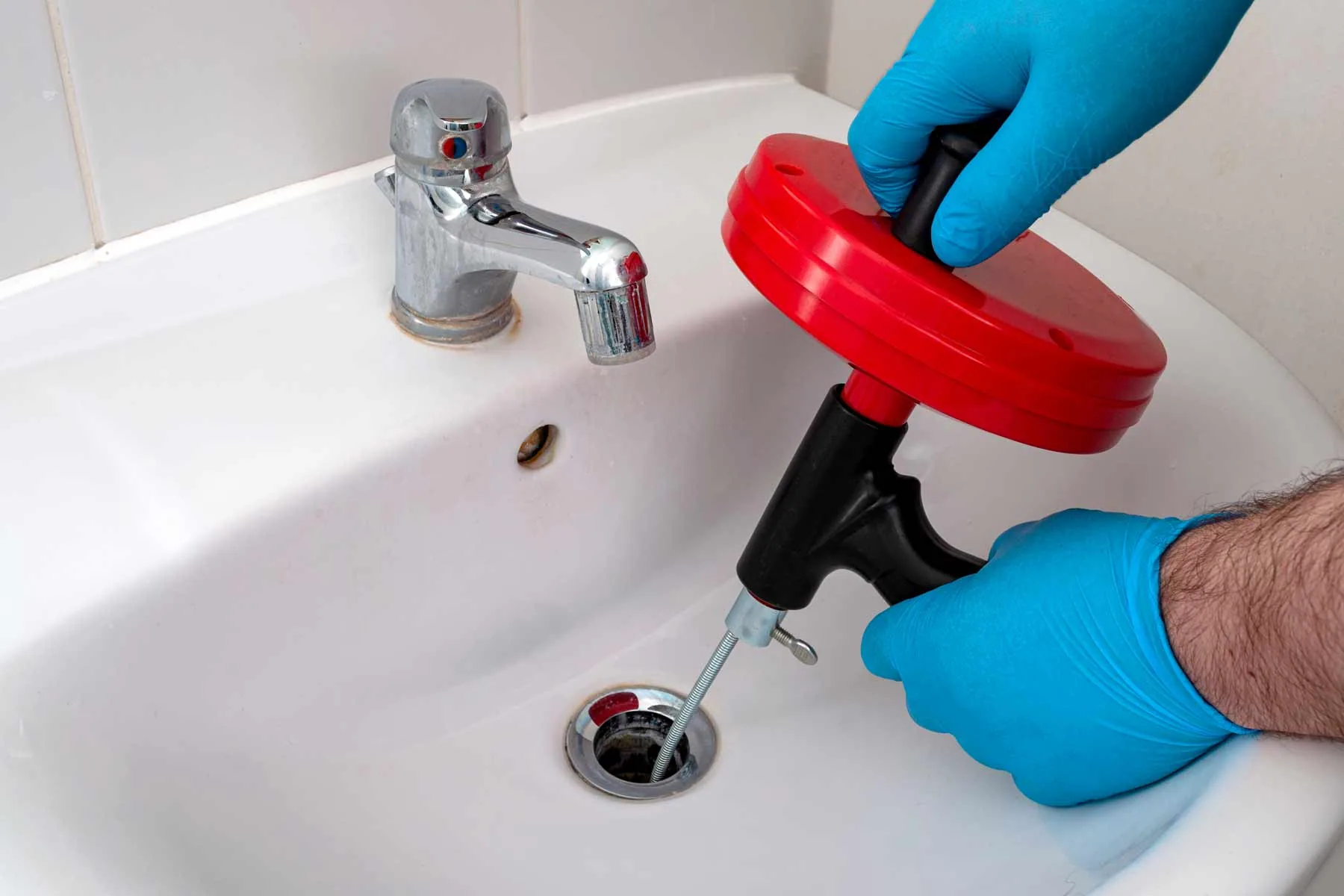 Blue gloved hands red drum auger white bathroom sink drain melrose stoneham